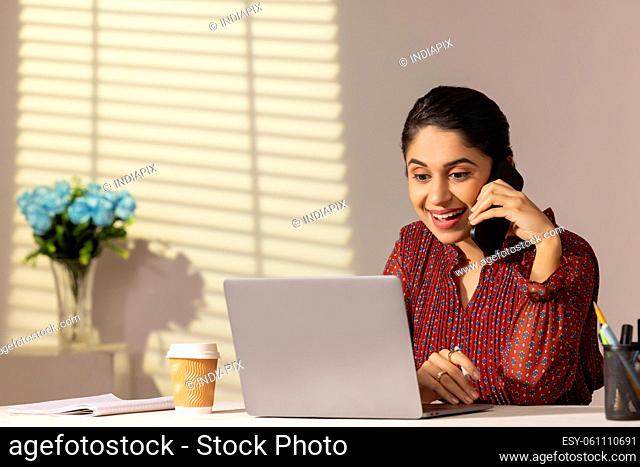 Portrait of a young working woman talking on Smartphone at her desk in office