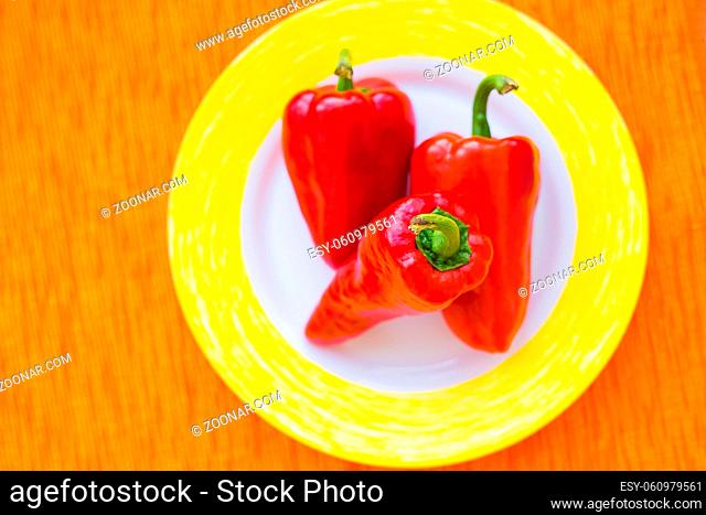 three red peppers on a colorful plate closeup