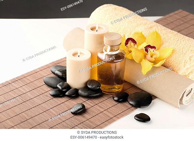 spa, health and beauty concept - closeup of essential oil, massage stones, candles and orchid flower