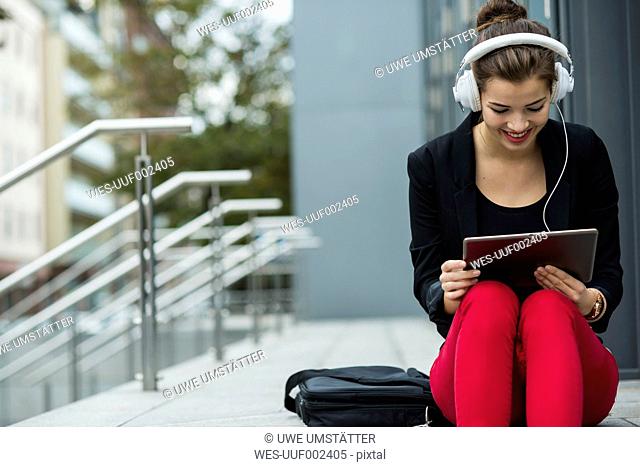 Young woman with headphones sitting on stairs using digital tablet