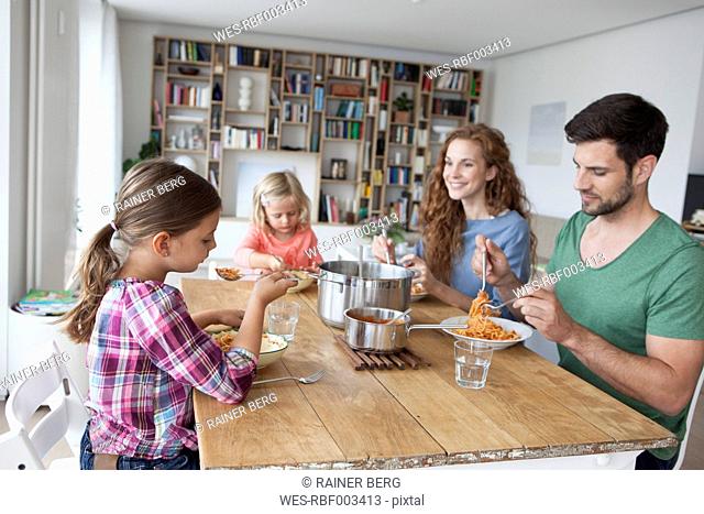 Little girl sitting at dining table with her parents and sister eating spaghetti