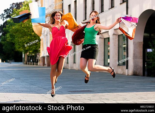 Two women being friends shopping downtown with colorful shopping bags, they are jumping for joy?
