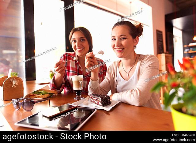 Toned image of happy best friends drinking coffee and eating sweet dishes while spending their free time in cafe or restaurant