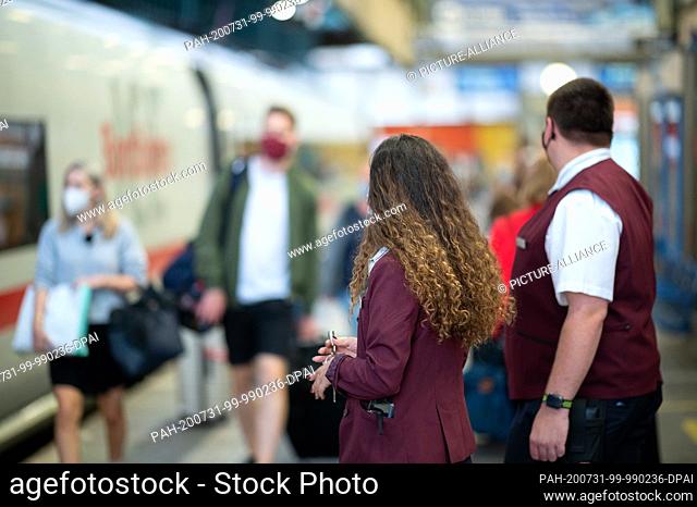 31 July 2020, Baden-Wuerttemberg, Stuttgart: Two train conductors in the new clothing of the Deutsche Bahn stand next to an ICE train that runs from Stuttgart...