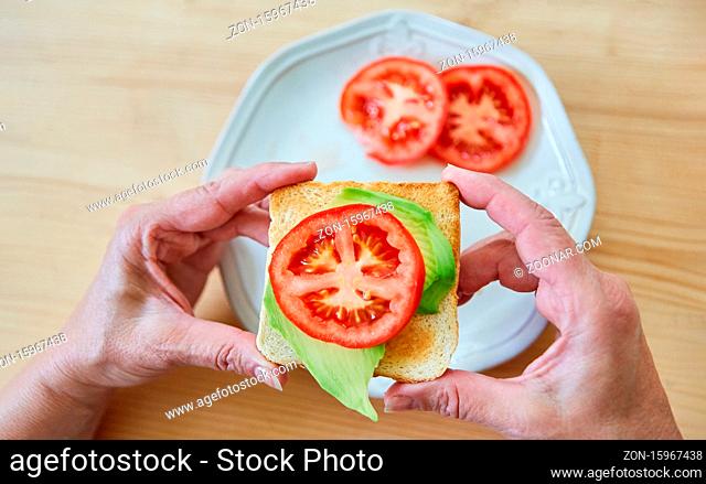 Hände halten einen veganen Toast mit Avocado und Tomate als gesunden Snack