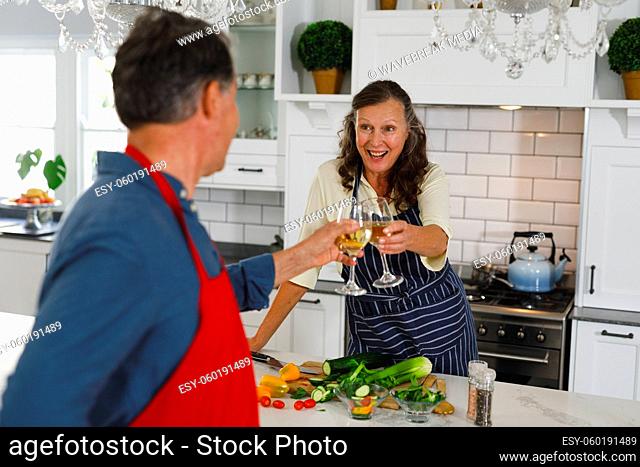 Happy senior caucasian couple in kitchen cooking together, drinking wine