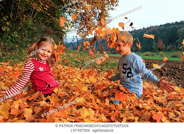 girl and boy playing in pile of leaves, fall Zuerich, Switzerland