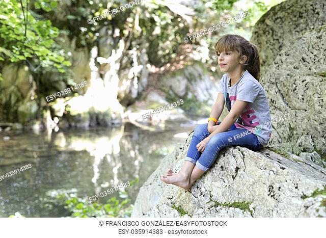 Girl sitting on a rock next to the Waterfall of the bucket in the Selva de Irati in Navarra, Spain