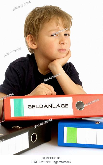 little boy seriously leaning on a file with the inscription 'Geldanlage' ('investment')