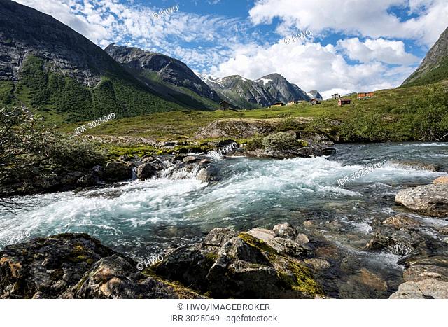 Torrent foaming between boulders in front of an alm or alpine meadow with huts and mountains