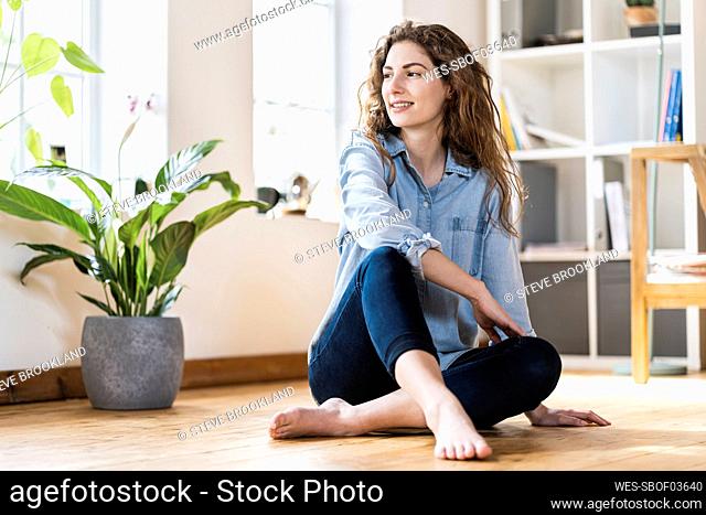 Smiling woman with long hair looking away while sitting on floor in living room