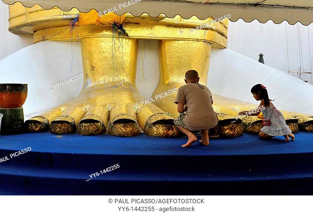 people praying at the feet of the Standing buddha knowns as luang pho at Wat Intharawihan, nakhon district of bangkok, thailand