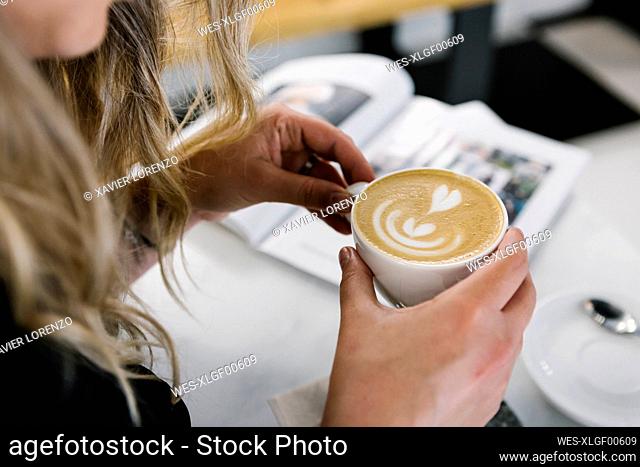 Woman holding cappuccino cup while sitting at coffee shop