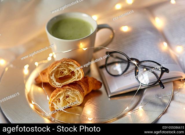 croissants, matcha tea, book and glasses in bed