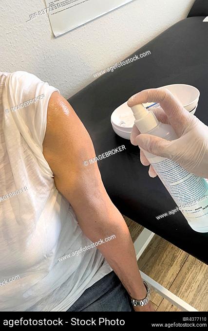 Patient's arm is disinfected by doctor's assistant with medical disinfectant spray Upper arm in front of injection for vaccination Booster against Covid-19...