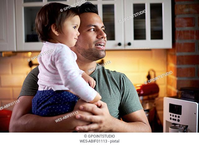 Father holding baby girl in kitchen at home