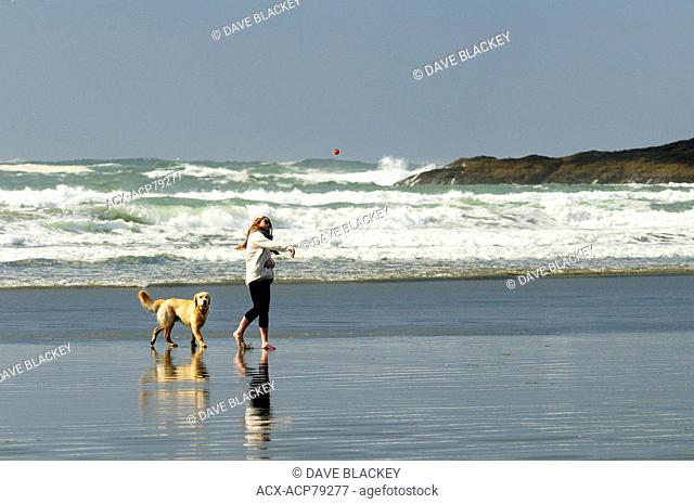 A young woman and her dog (a Golden Retriever) playing with a ball on Chesterman Beach near Tofino, BC
