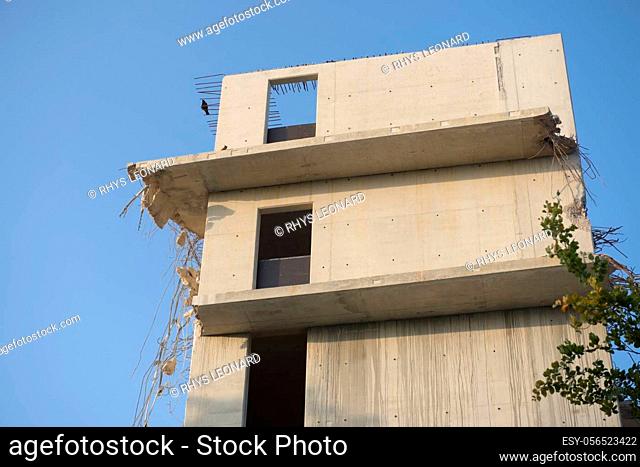 Plain blue background behind the top three floors of an empty concrete building. Partly wrecked and demolished as steel supports hang out with rubble