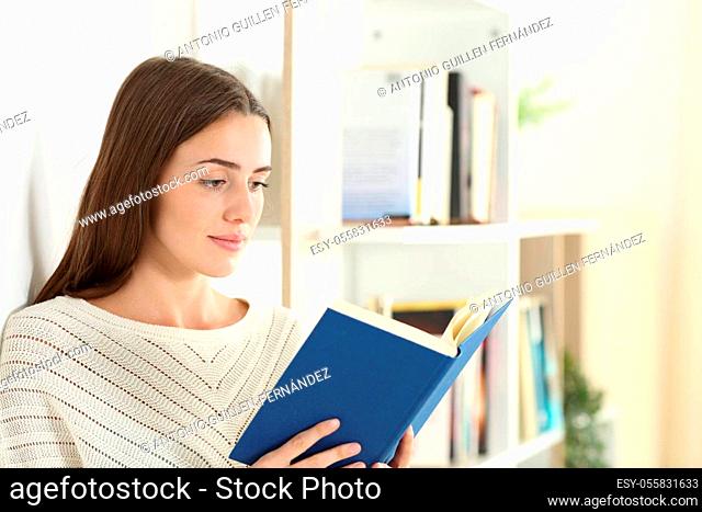 Serious teen reading a paper book standing in the living room at home