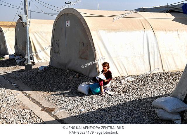 A girl sits with a schoolbook for math and studies by her family's tent in the Mamilian refugee camp in the Dohuk region, Iraq, 19 October 2016