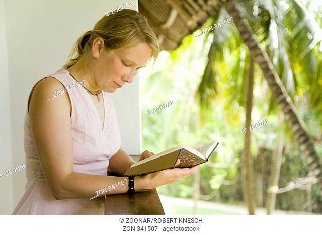 Blonde Frau liest auf einem Balkon in ihrem Tagebuch Model: Lara