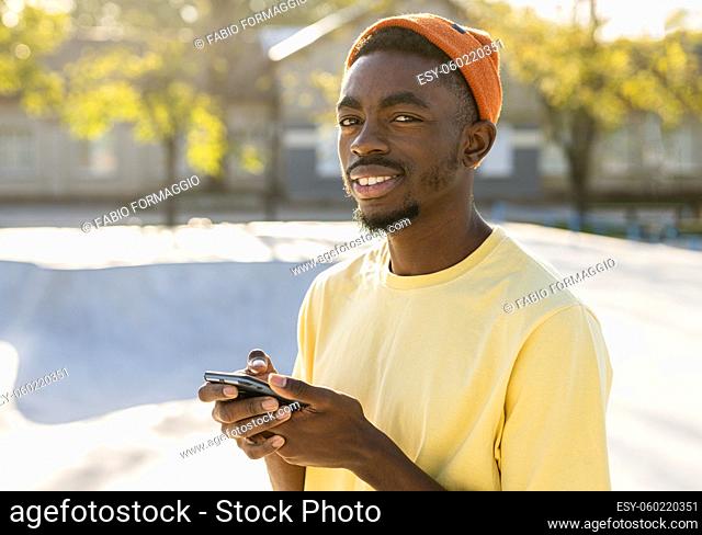 Stylish cool teen male skateboarder at skate park using smartphone