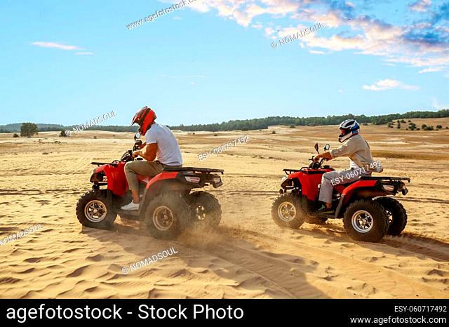 Two men in helmets ride on atv in desert. Male persons on quad bikes, sandy race, dune safari in hot sunny day, 4x4 extreme adventure, quad-biking