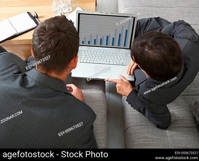 Business meeting at office. Youing businsspeople sitting on sofa, looking at financial charts on laptop screen. Overhead view