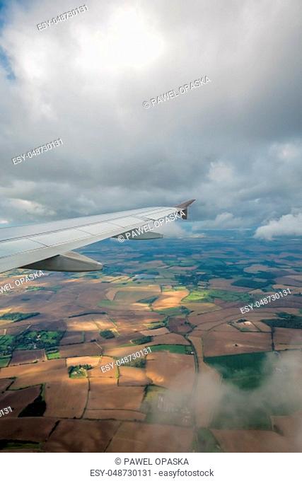 Window view of the wing of an airplane flying above the clouds and english countryside