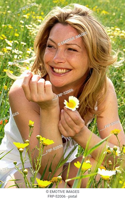 Woman is sitting in a meadow and is playing with a flower