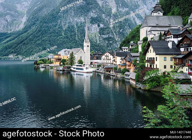 famous lake side view of hallstatt village with alps behind, foliage leaves framed. austria
