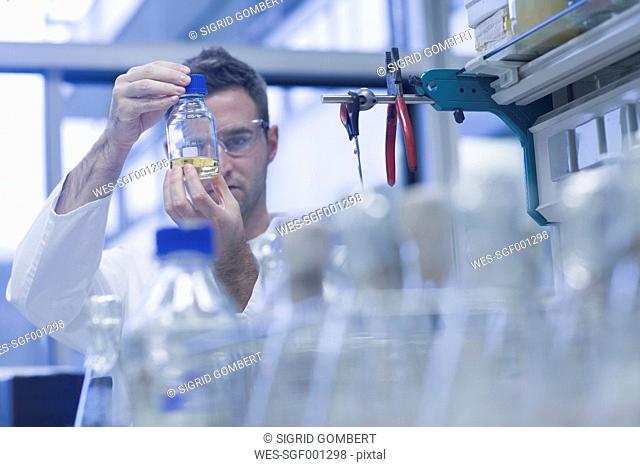 Scientist in microbiological lab looking at liquid in bottle