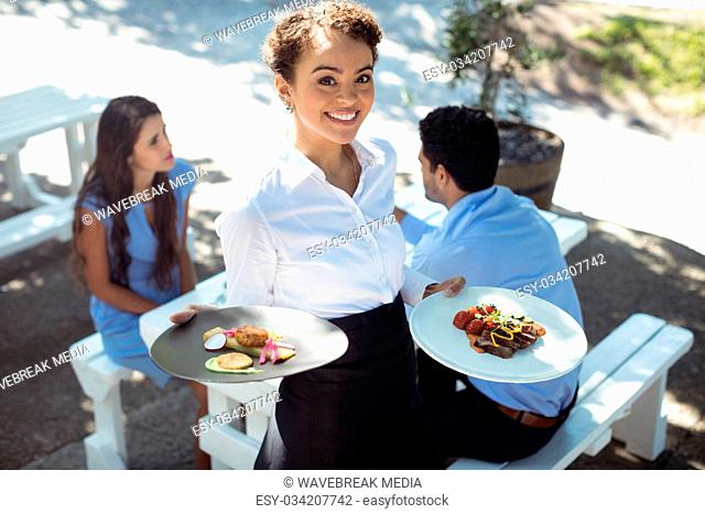 Smiling waitress holding delicious food in kitchen