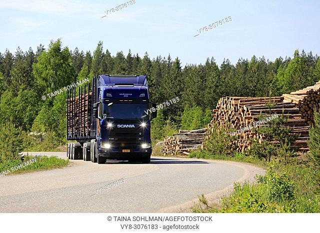 Blue Next Generation Scania R730 XT logging truck on road test by forest logging site with shiny high beams on briefly on Scania Tour 2018 in Lohja