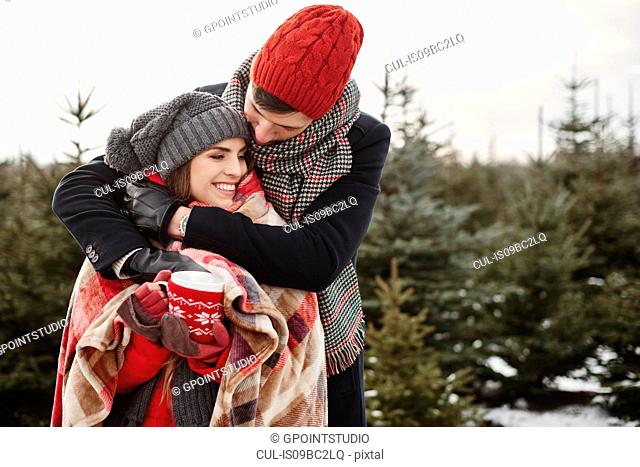 Romantic young couple in christmas tree forest wrapped in blanket