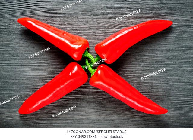 X shaped figure made of four ripe sweet red Kapia peppers on dark shale stone background