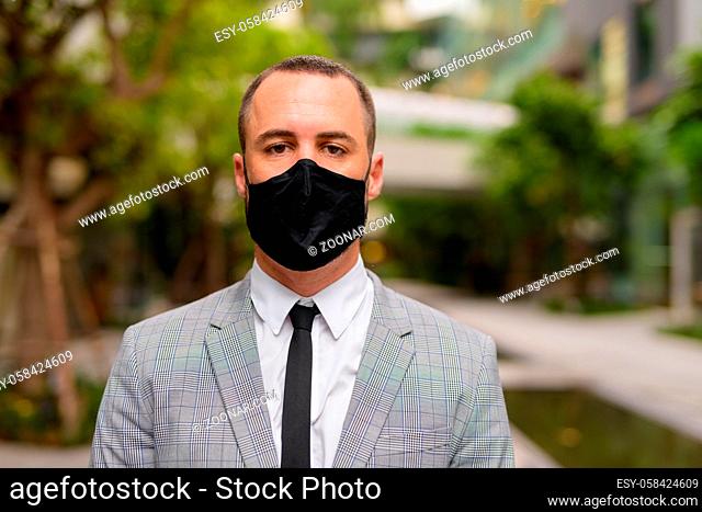Portrait of Hispanic bald businessman with mask for protection from corona virus outbreak in the city with nature outdoors