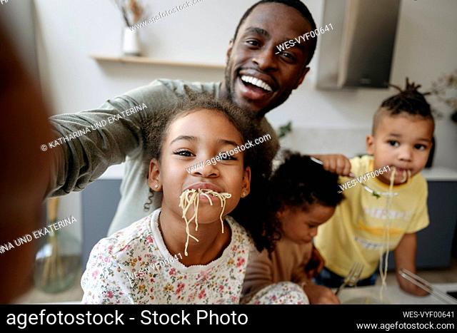 Happy man taking selfie with daughter and sons having spaghetti in kitchen