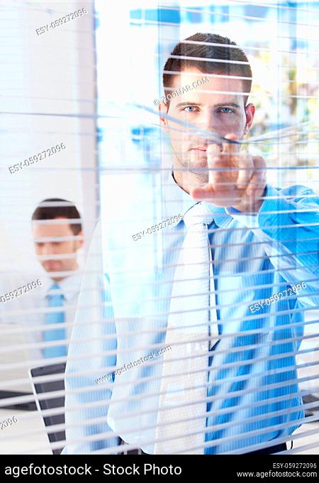 Handsome young businessman peeping through blind from bright office