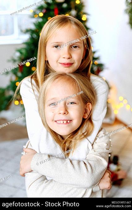 Smiling sisters embracing with Christmas tree in background at home
