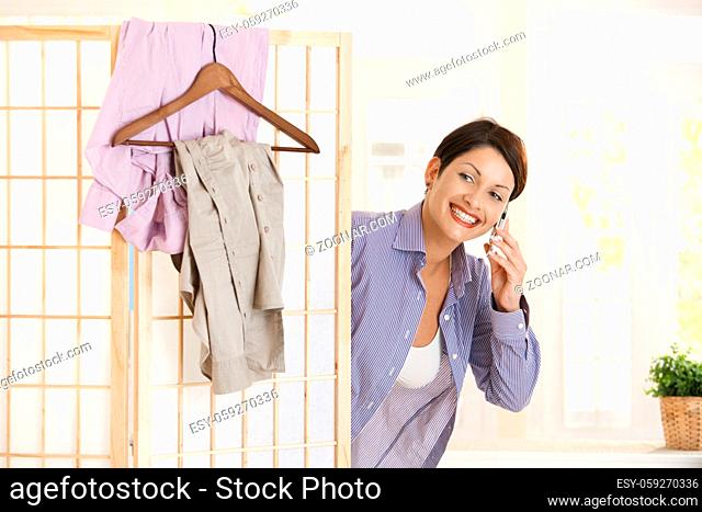 Happy young woman talking on mobile phone while dressing up in the morning, smiling
