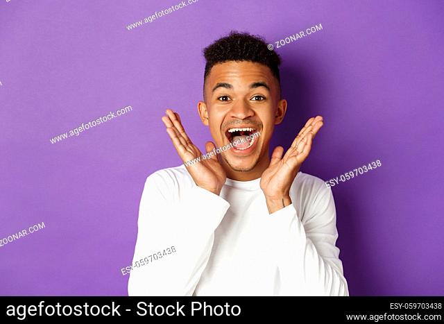 Close-up of excited african-american man, scream of joy and looking amazed at camera, hear good news, standing over purple background