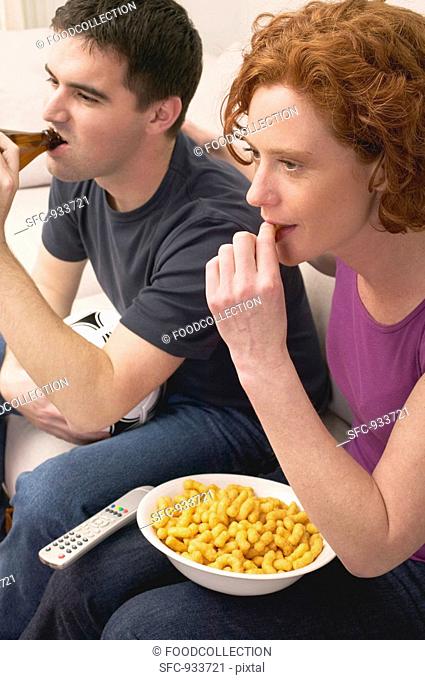 Young couple with football, beer and snack food watching TV