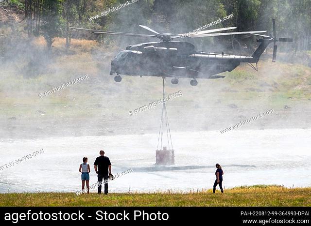 12 August 2022, Saxony-Anhalt, Elend: A Bundeswehr CH-53 helicopter takes water from the Mandelholz reservoir to fight a forest fire near Schierke