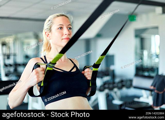 Sportliche Frau macht Rückentraining mit Schlingen an Zugstation im Fitnessstudio