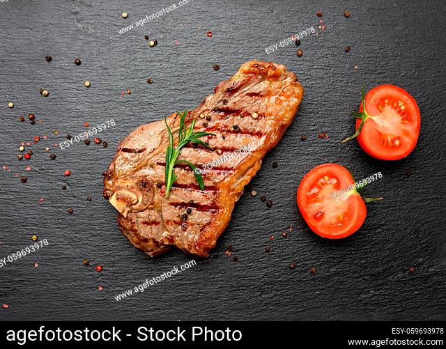 whole fried New York beef steak on a black board, striploin doneness rare, top view