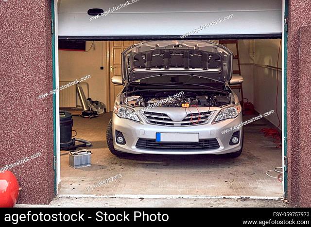 Car in a small repair shop garage with open hood, engine diagnostics