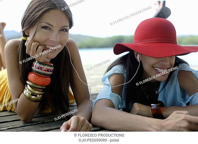 Two women lying on dock with earbuds