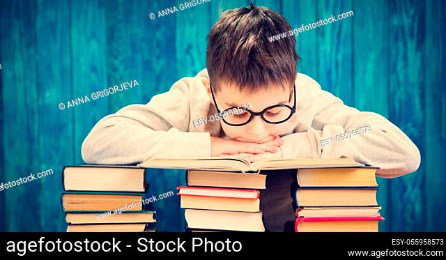 eight years old child reading a book at home. Boy studying at table on blue background