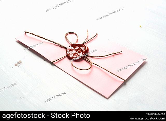 Pink letter envelope with wax seal on wooden surface